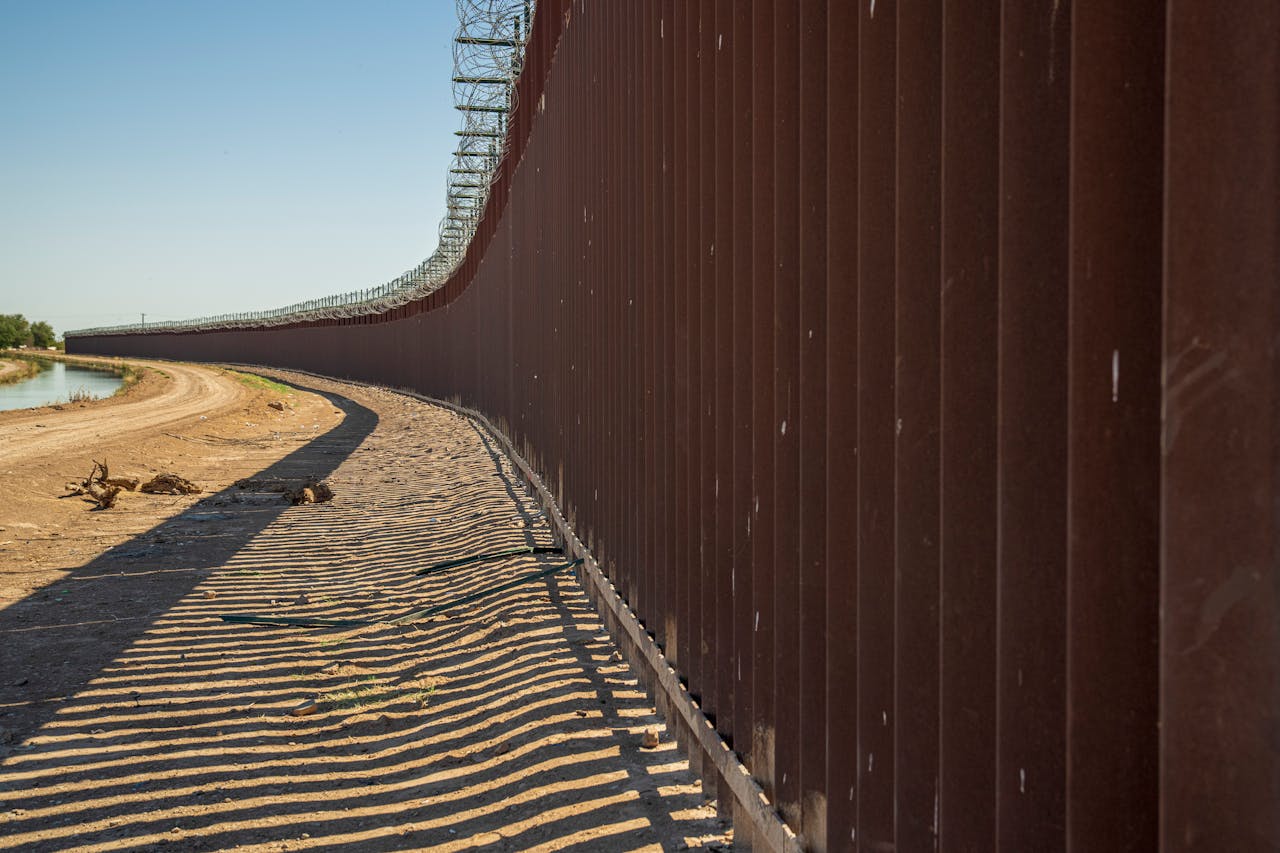 Long view of a steel border wall under clear skies, emphasizing solitude and division.