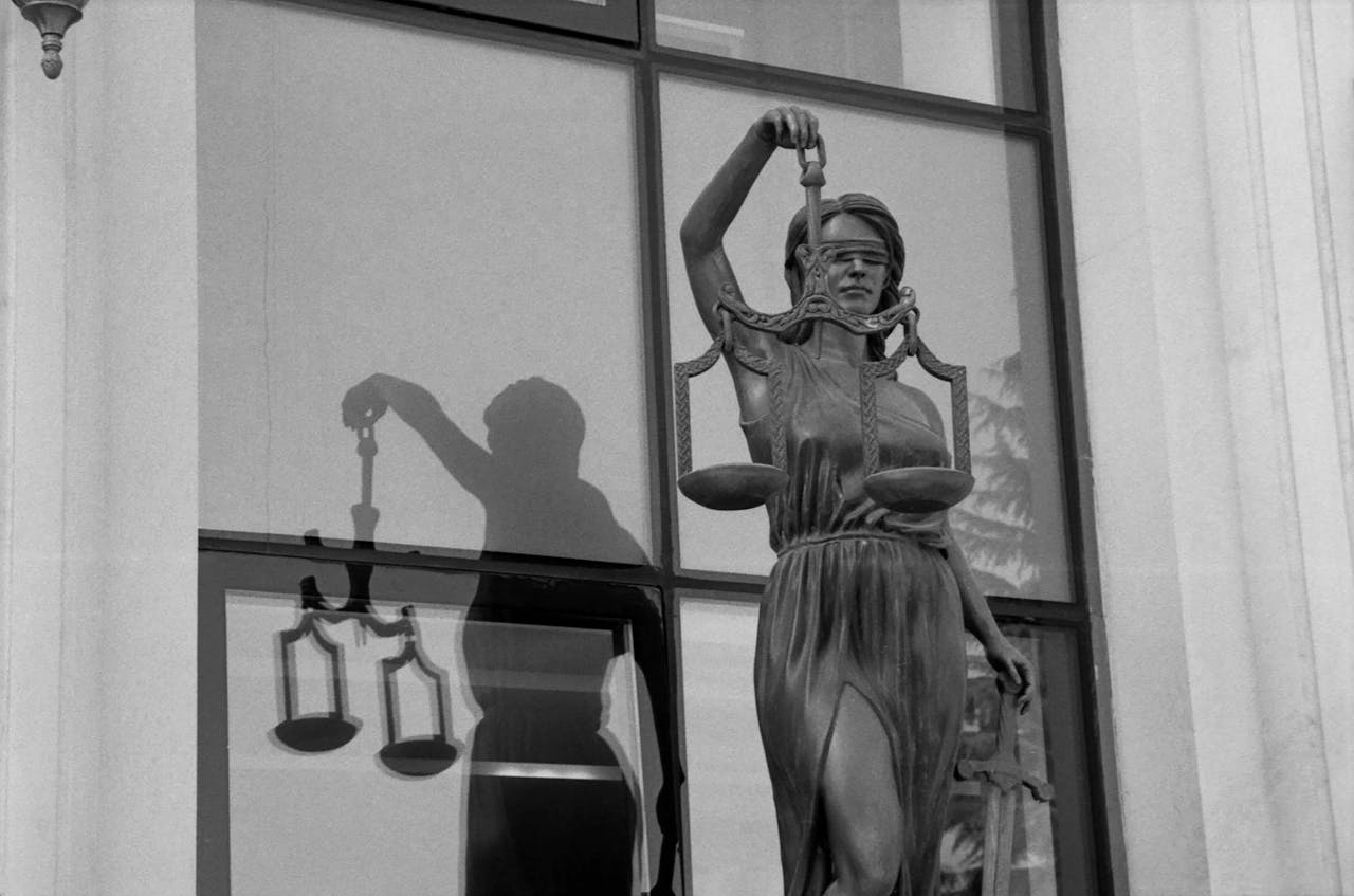 Black and white image of Lady Justice statue reflecting in a window, symbolizing fairness.